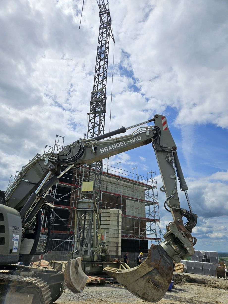 Bagger im Vordergrund mit einer Baustelle und einem Krahn im Hintergrund